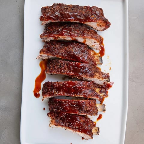 Juicy BBQ Ribs with a dark, smoky barbecue glaze sit on a platter, garnished with fresh parsley and ready for a backyard feast.