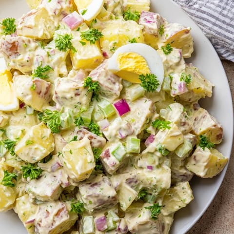 Chilled homemade potato salad garnished with fresh parsley and chopped hard-boiled eggs, served in a white bowl.