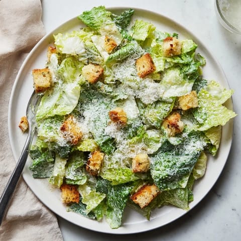 Crisp Caesar salad served in a wooden bowl with extra black pepper and shaved Parmesan cheese.