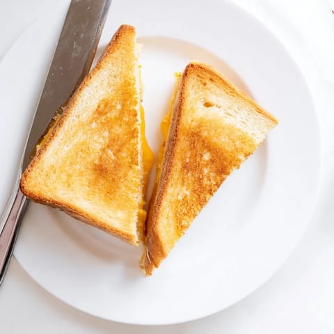 Two crispy Grilled Cheese Sandwich halves dipped in creamy tomato soup on a rustic wooden table.